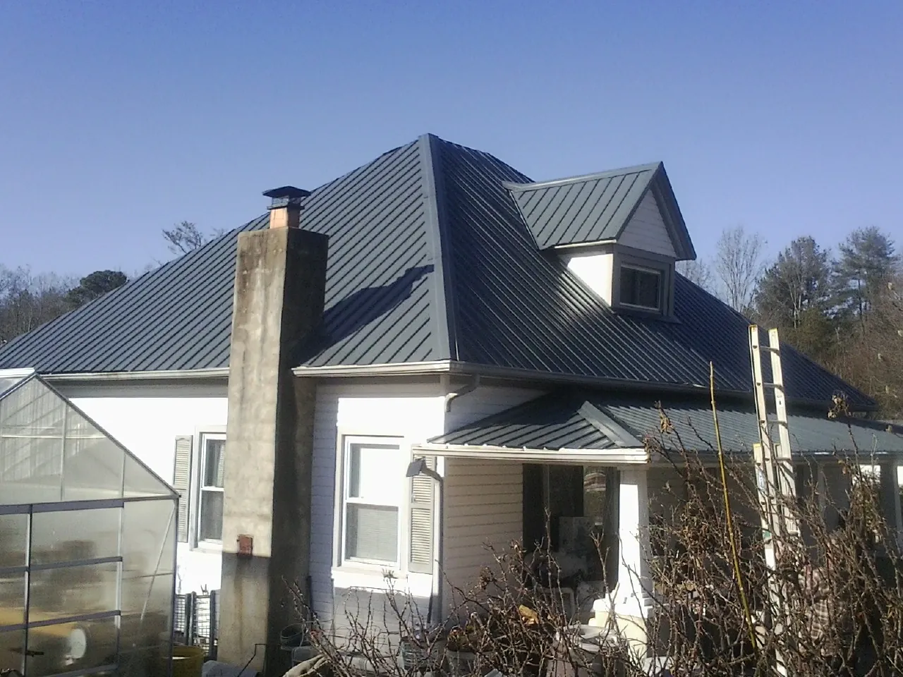 Dark blue standing seam metal roof on a white farmhouse with dormer — Slate & Tile Roof Repair by Roofing Brothers in Brice