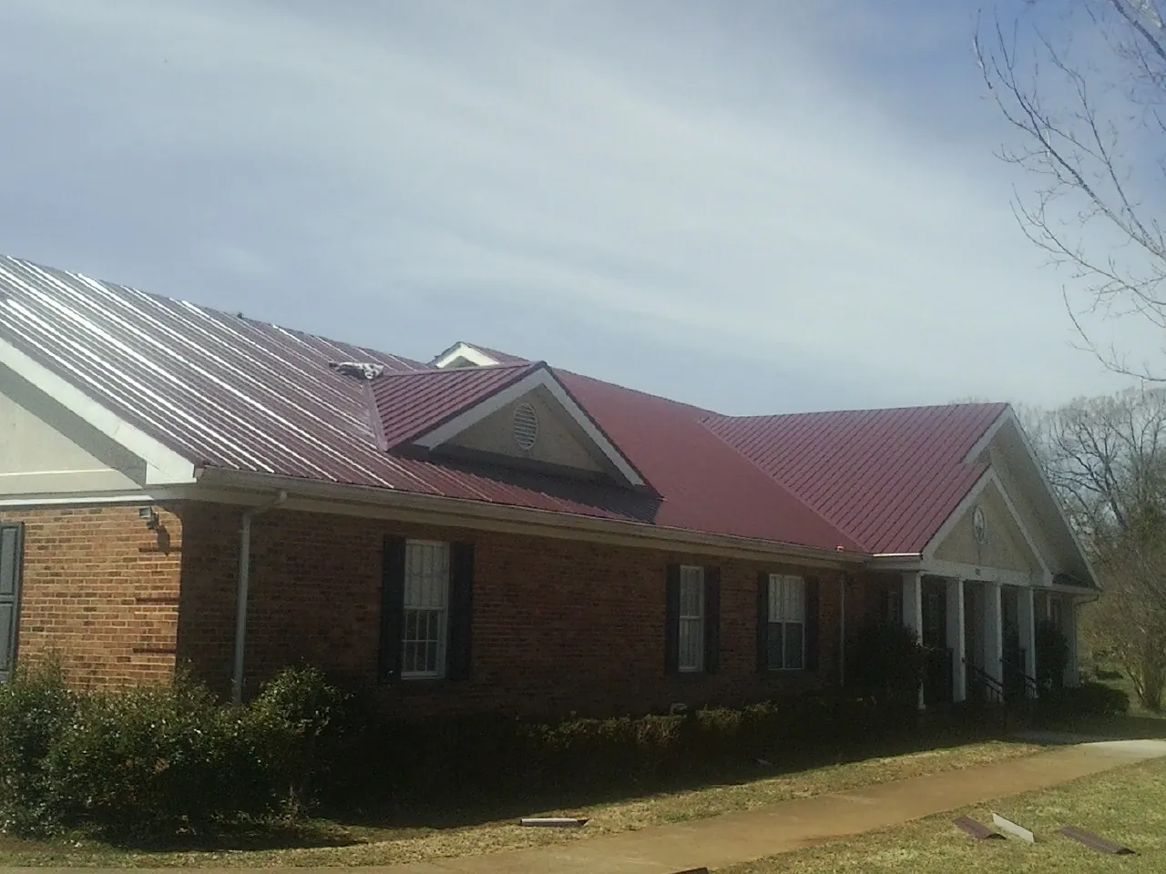 Red metal roof with gabled entries on a long brick building, from a Hail Damage Roof Repair job in Brice
