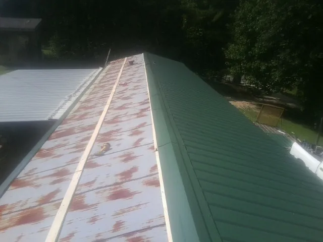 Old rusted panels beside newly installed green metal roofing — Wind Damage Roof Repair by Roofing Brothers in Brice