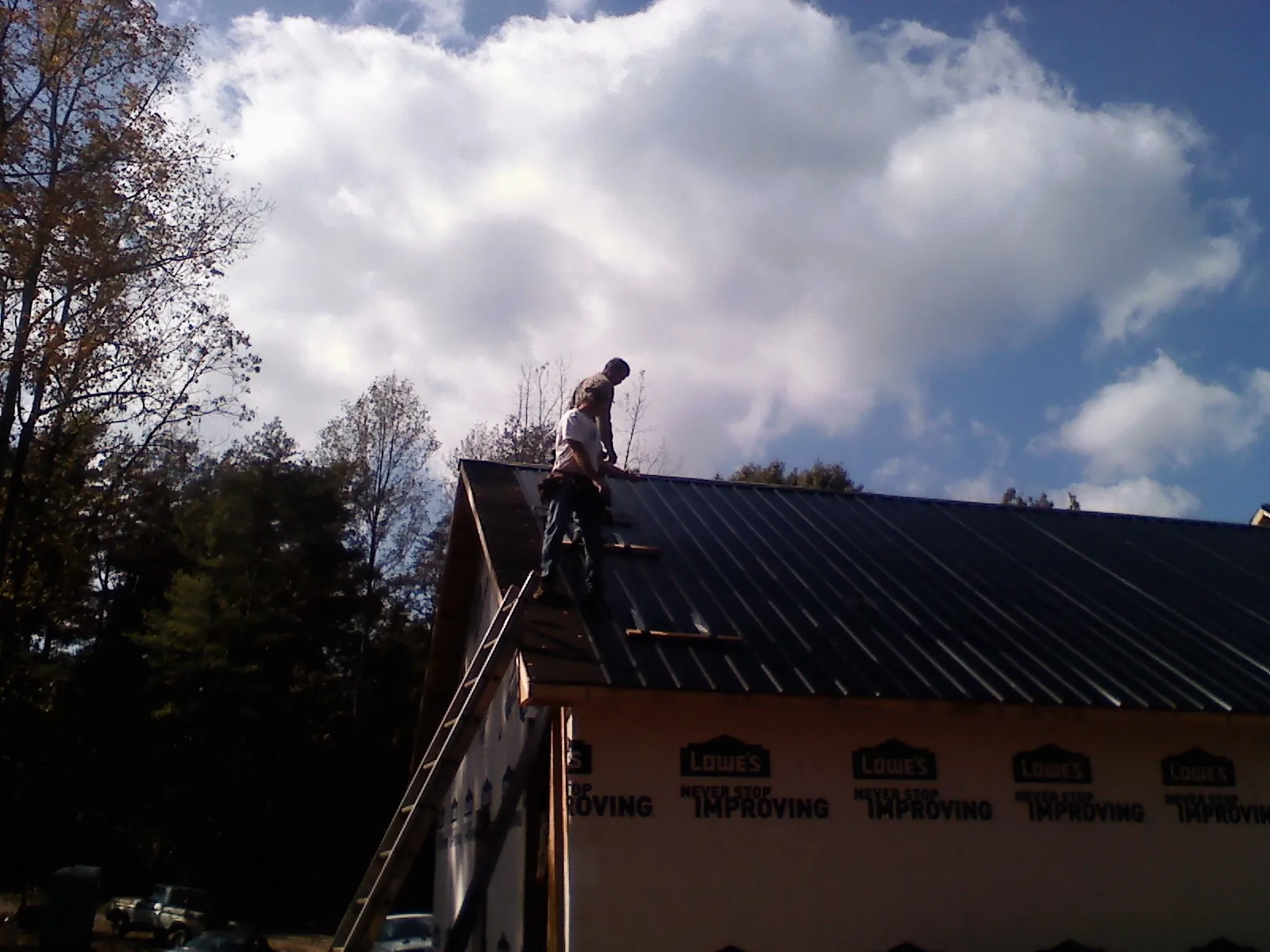 Roofer fastening dark metal panels high against a cloudy sky, from a Roof Inspection job in Brice