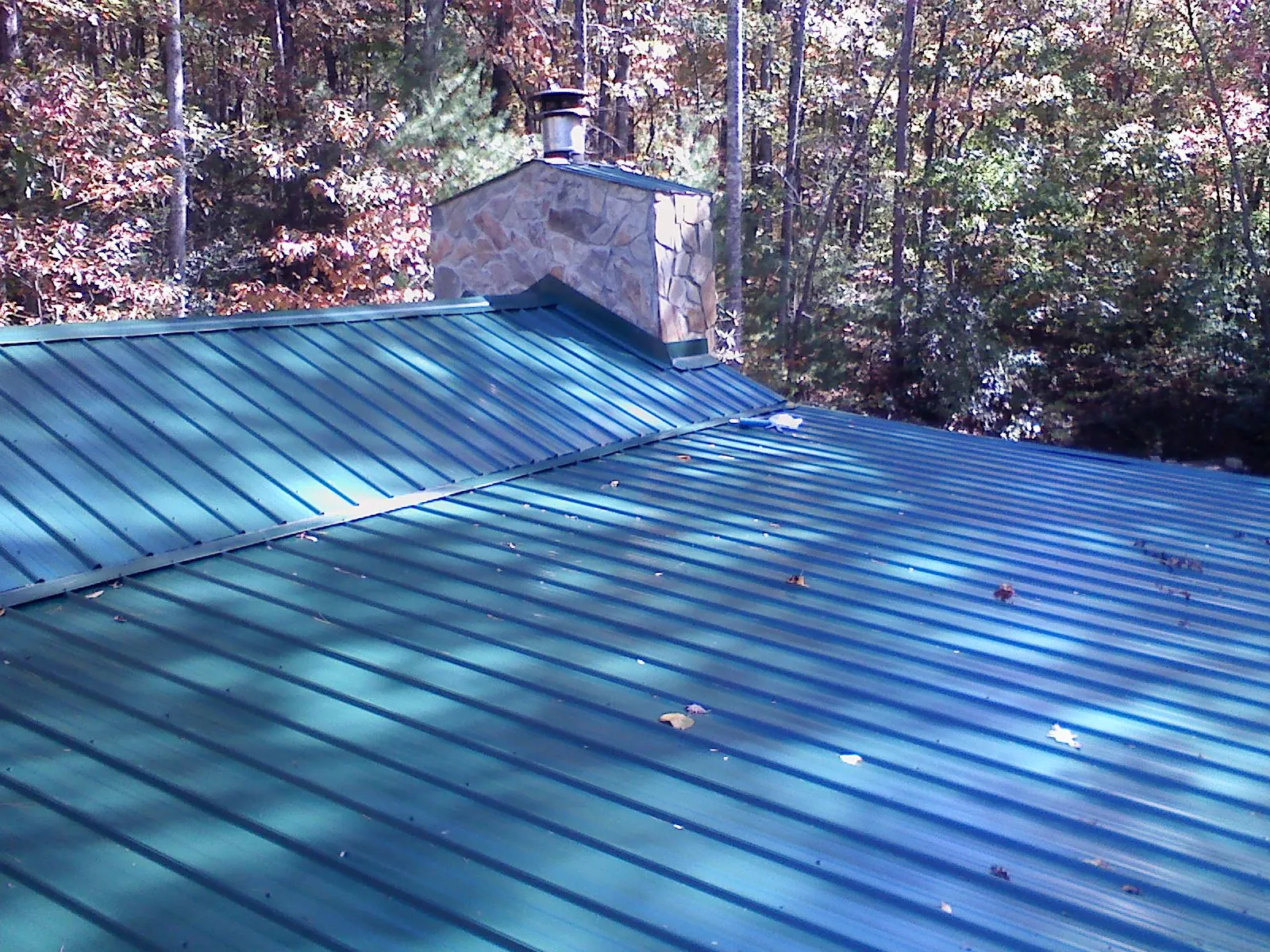 New green metal roof and stone chimney surrounded by autumn woods in Brice