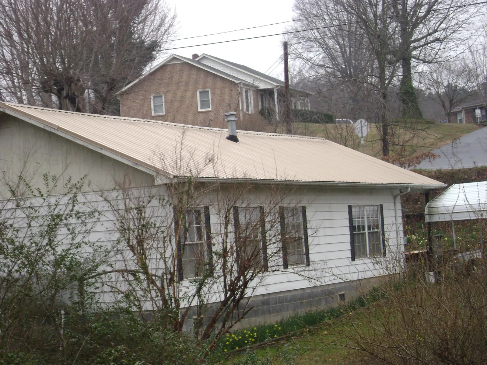 Tan metal roof on a white sided house set into a hillside — Commercial Roofing by Roofing Brothers in Brice