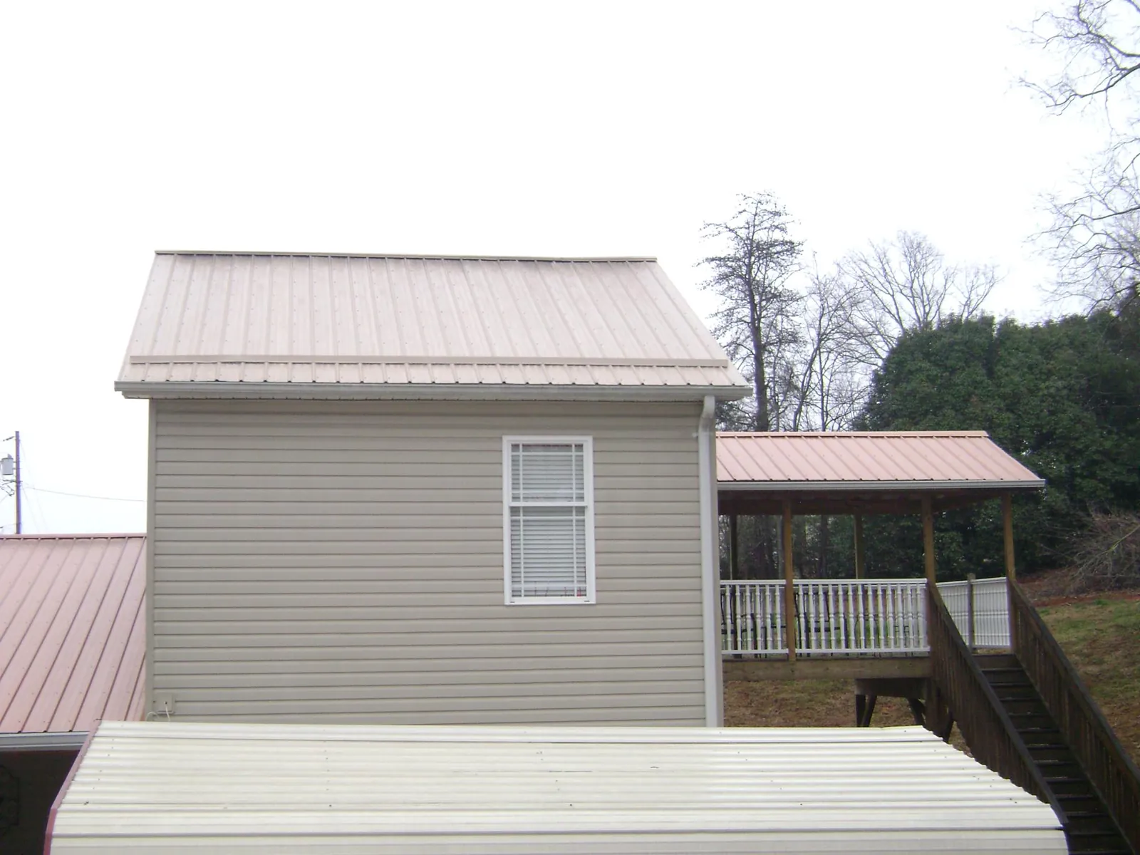 Tan metal roofs on a two story addition and attached porch, from a Roof Replacement job in Brice